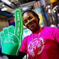 A woman in a pink t-shirt holding a large green foam finger.