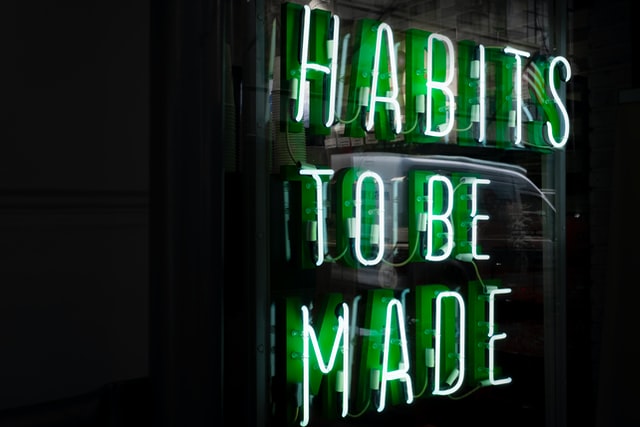 White and green fluorescent lights on a black background spell out "habits to be made".