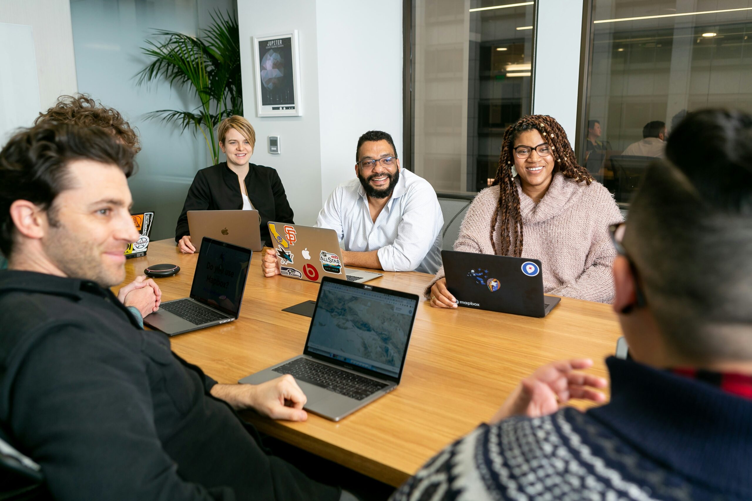 four people with laptops two men and two women listen to person talking in a meeting